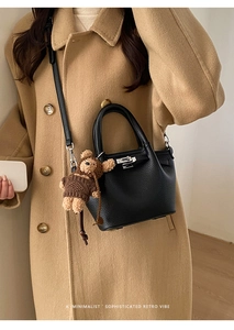 Detail of black lychee grain leather bucket bag with silver lock and teddy bear charm