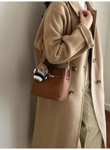 Detailed view of brown litchi grain leather bucket bag featuring a cute teddy bear charm