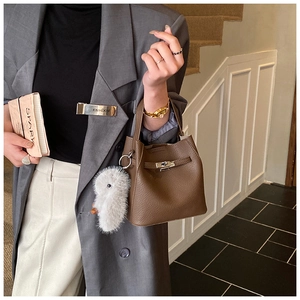 Detail of a brown lychee pattern leather bucket bag with clasp and rabbit charm