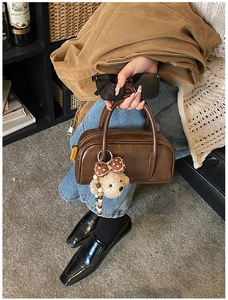 Détail d'un sac Boston en cuir marron foncé avec charme ours en peluche et fini brillant