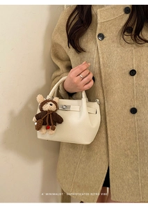 Detail of cream bucket bag with lychee grain leather, metal buckle and bear charm