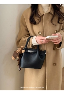 Detail of black lychee grain leather tote bag with silver lock and plush bear charm