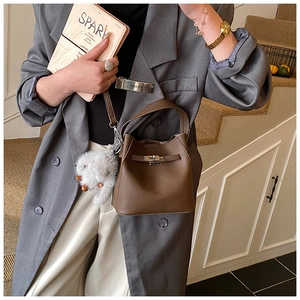 Detail of a brown lychee leather bucket bag with silver lock and plush bunny charm