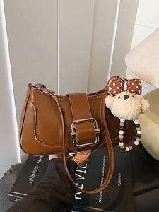 Brown vintage baguette bag with silver buckle and plush bear pendant on a book