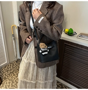 Detail of black pebbled leather bucket bag with silver lock and plush bear charm decoration