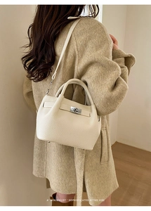 Close-up of cream leather bucket bag with silver clasp styled on a camel wool coat