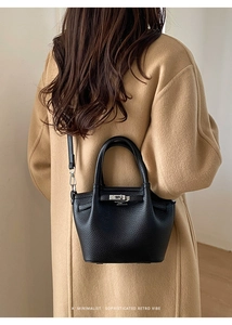 Detail of black pebbled leather bucket bag with silver buckle worn with wool coat