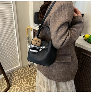Detail of black lychee grain bucket bag featuring a cute brown teddy bear keychain