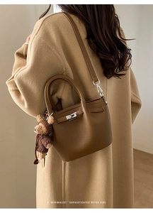 Brown litchi grain leather tote bag with silver lock and plush bear on a khaki coat