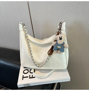 Détail du grand sac hobo crème avec chaîne argentée et breloque ours sur un livre