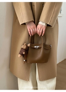Detail of brown litchi pattern leather bucket bag with metal lock and plush bear charm