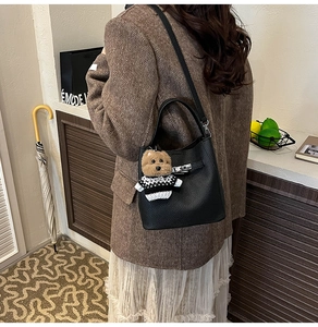 Detail of black pebbled leather bucket bag with silver turn-lock and cute bear charm