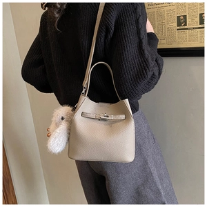 Detail of beige lychee pattern bucket bag with metal lock and cute plush animal charm