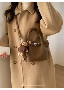 Brown litchi pattern leather bucket bag with cute bear charm worn on cashmere coat