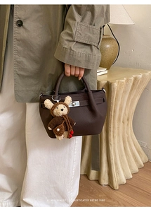 Detail of dark brown lychee leather bucket bag with metal turn-lock and cute bear charm