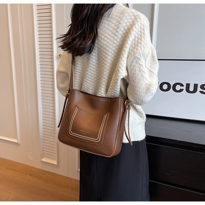 Détail du sac seau en cuir marron avec texte tendance et bandoulière réglable