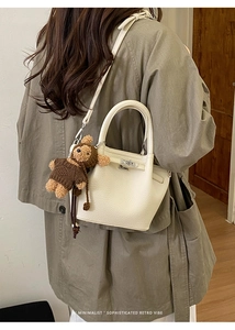 Detailed shot of white lychee leather bucket bag with silver lock and plush bear charm