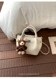 Close-up of cream textured leather bucket bag with metal lock and cute bear charm