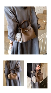 Detail of dark brown pebble leather bucket bag with metal clasp and plush white charm