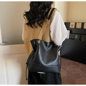 Detail of a black quilted bucket bag with gold chain strap and drawstring closure
