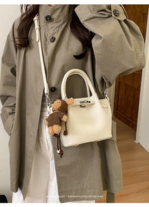 Detail of cream leather handbag with top handle and brown bear charm on trench coat