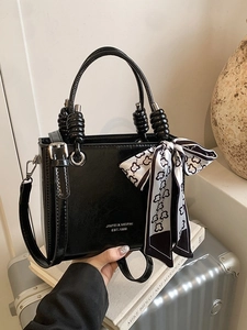 Elegant black glossy bucket bag with pearl-beaded handles and decorative silk scarf