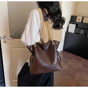 Deep brown bucket bag with geometric stitching and gold chain strap on model