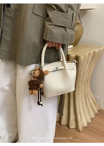 Detail of white lychee leather handbag with metal lock and cute bear plush charm