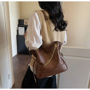 Detail of dark brown quilted bucket bag with gold chain strap and drawstring closure