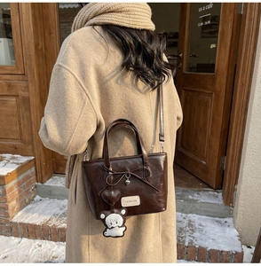 Detail of dark brown leather bucket bag with bow, metal heart and plush bear charm