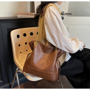 Close-up of brown leather bucket bag with geometric stitching and gold chain strap