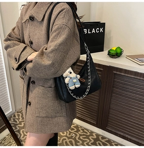 Détail du sac hobo noir en PU avec chaîne argentée et charm ours sur un manteau à carreaux