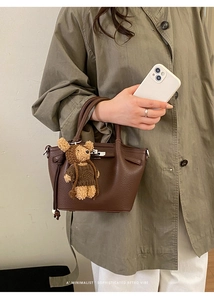 Detail of dark brown pebble leather handbag with cute teddy bear charm on model