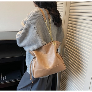 Detail of light brown bucket bag with white contrast stitching and gold chain strap