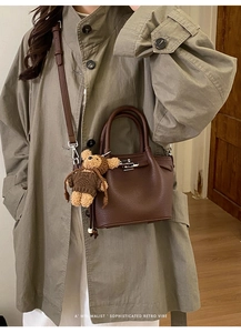 Detail of dark brown lychee grain leather tote with silver lock and bear charm accessory