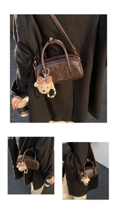 Détail d'un sac bowling en cuir marron foncé avec finitions dorées et breloque ours