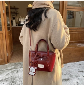 Detail of burgundy patent leather bucket bag with bow, heart charm and bear pendant