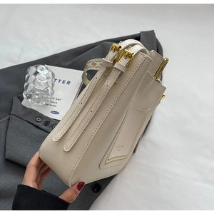 Détail du sac seau crème montrant des boucles dorées et une bandoulière tissée rétro