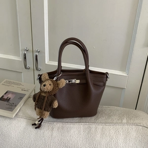 Detail of dark brown lychee grain leather tote with metal turn-lock and teddy bear charm