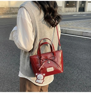 Detail of red patent leather bucket bag with bow, heart charm and bear keychain accessory