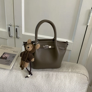 Detail of coffee brown lychee leather handbag with silver turn-lock and cute bear charm