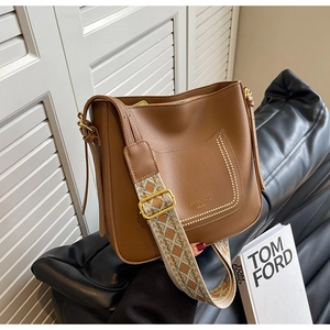 Gros plan d'un sac seau en cuir marron avec bandoulière tissée et volets blancs