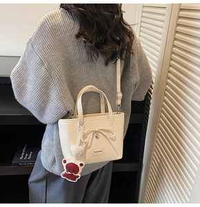 Detail of white bucket bag with bow, heart pendant, and brown teddy bear charm on model