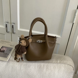 Detail of brown lychee leather bucket bag with silver twist lock and cute bear charm