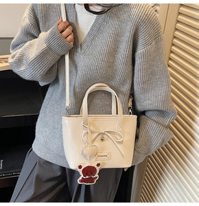 Detail of cream-colored bucket bag with bow, heart pendant and brown bear charm decoration