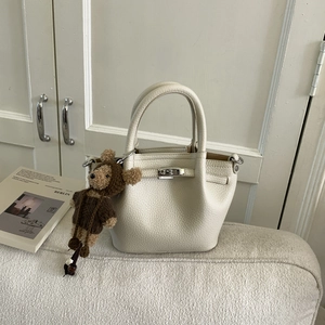 Detail of cream lychee leather tote bag with silver hardware and cute teddy bear charm