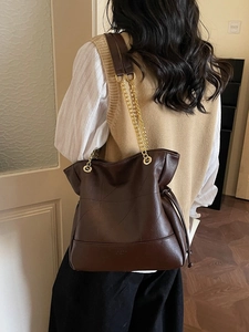 Dark brown leather bucket bag with geometric stitching and gold chain strap on shoulder