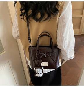 Detail of dark brown faux leather bucket bag with bow decoration and cute bear charm