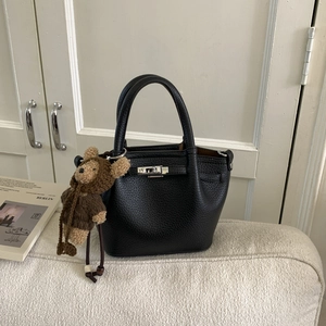Close-up of black lychee leather handbag with silver lock and a cute bear charm