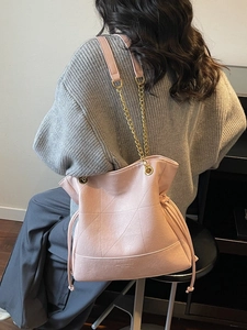 Pink quilted bucket bag with gold chain strap carried by a model in casual attire